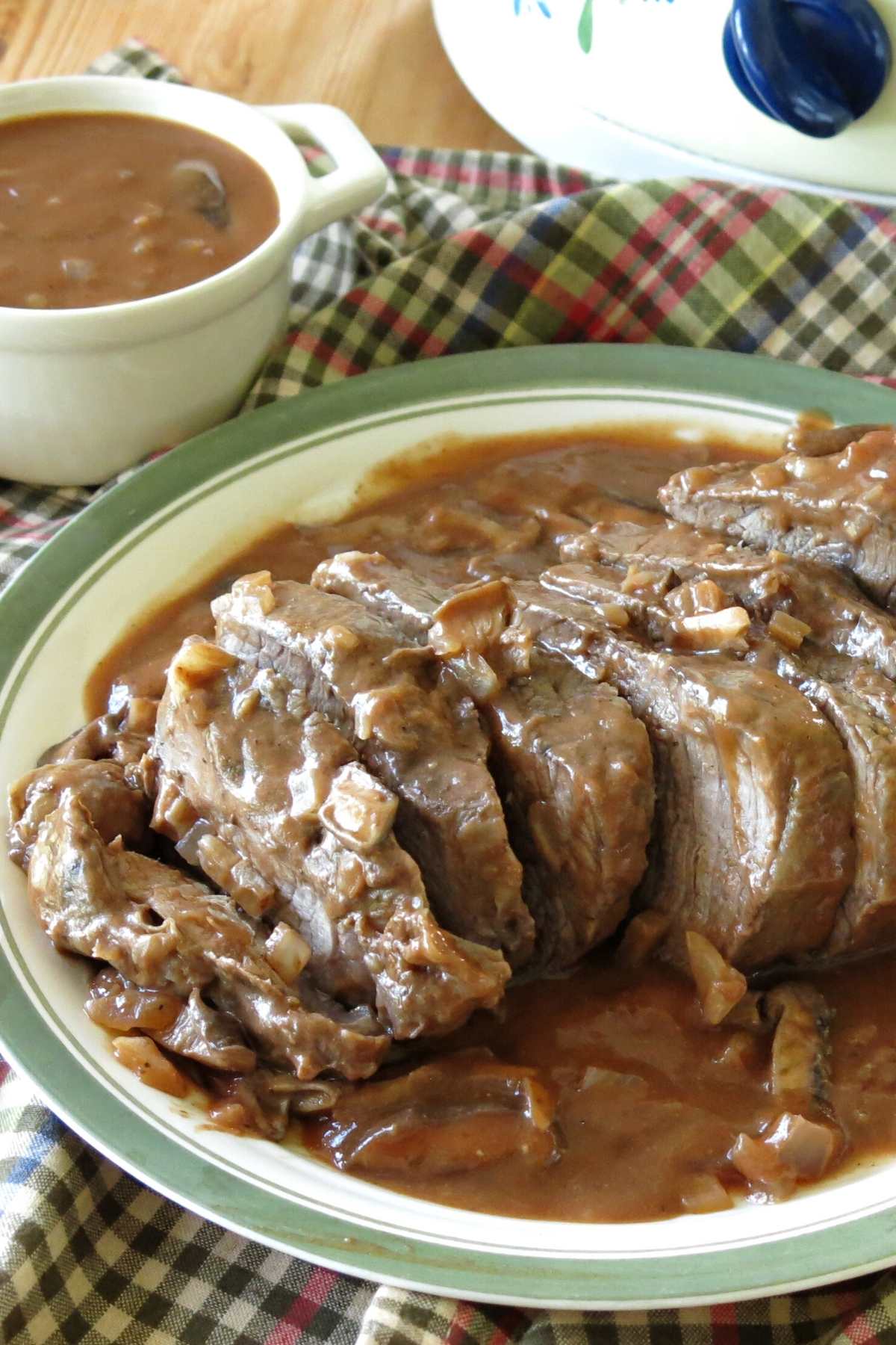 Slow Cooker Beef Shoulder Roast topped with mushroom wine sauce on plate with crock-pot behind it.