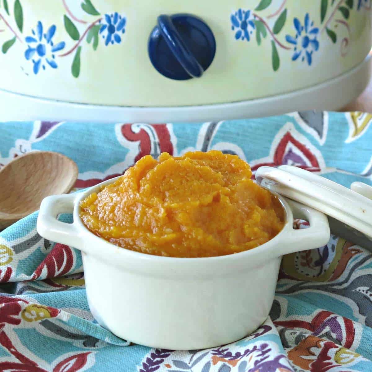 A cup of pureed butternut squash in front of a crock-pot.