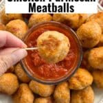 A baked chicken parmesan meatball on a toothpick over a plate with more meatballs and marinara.