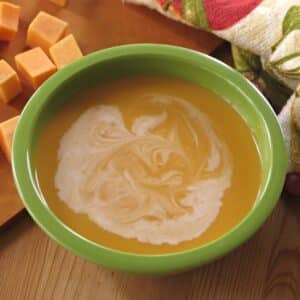 Creamy butternut squash soup with orange juice in a bowl surrounded by cubes of butternut squash.