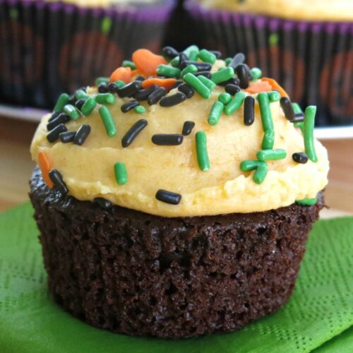 Chocolate pumpkin cupcakes with pumpkin buttercream frosting topped with green, chocolate and orange sprinkles.