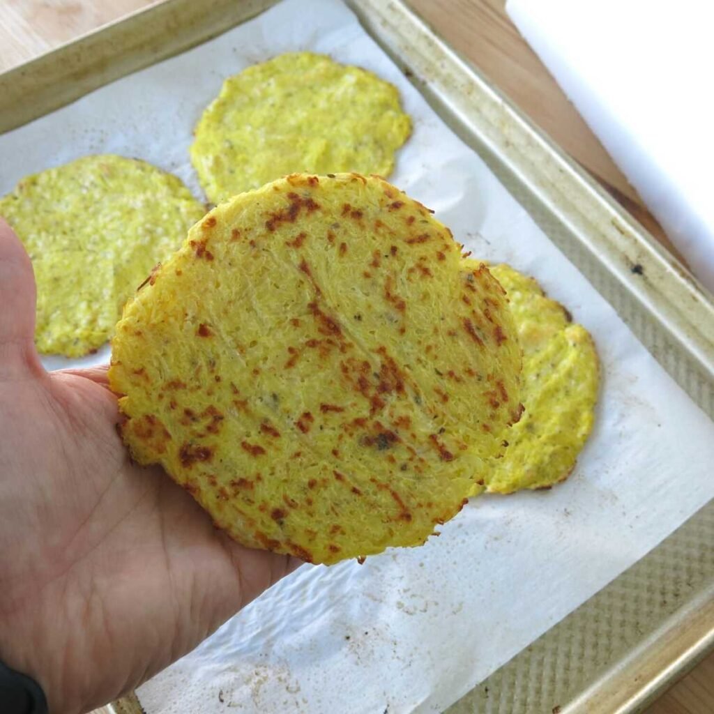 Hand holding a cooked spaghetti squash pizza crust to show the browned underside.