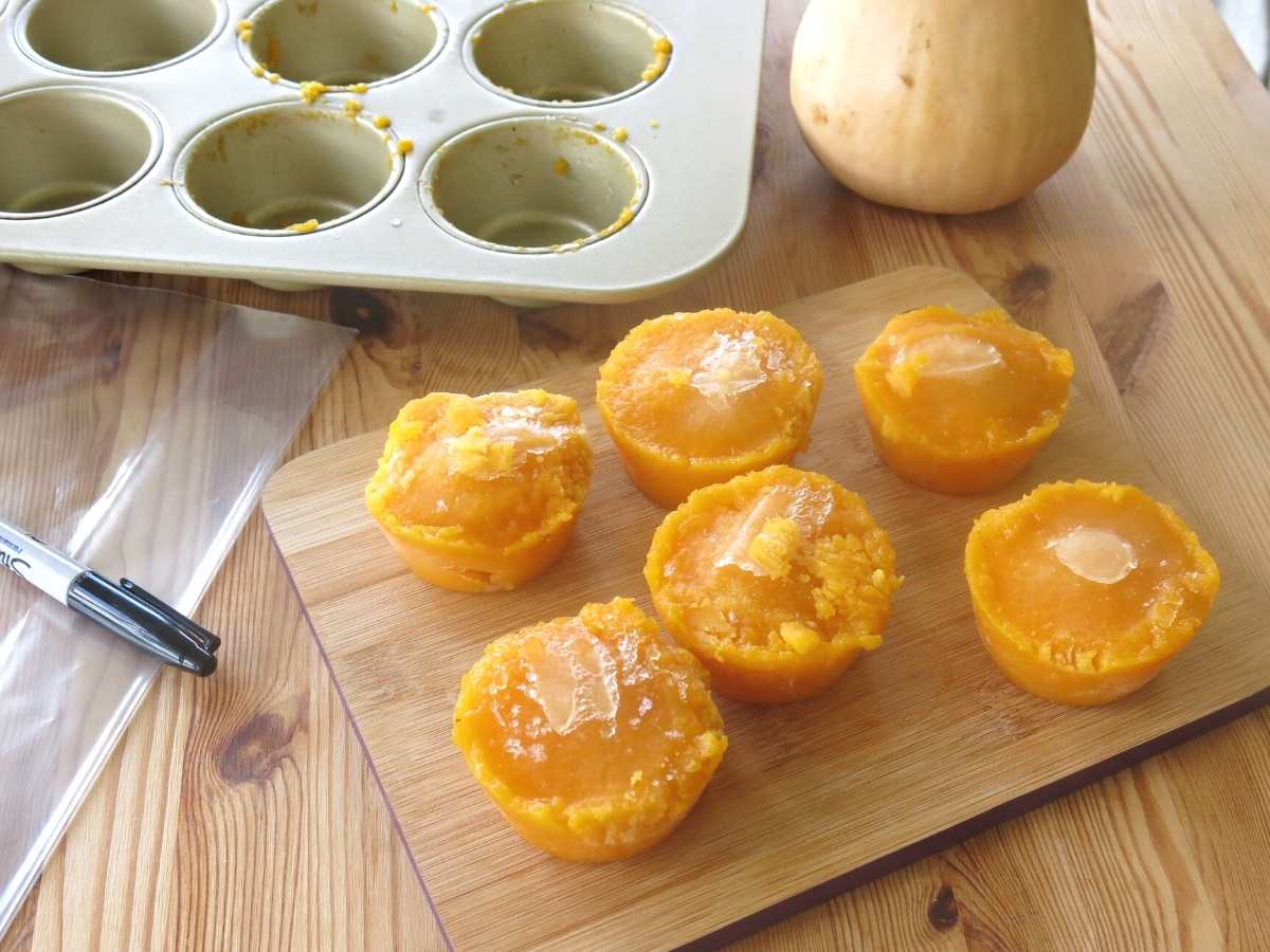 Frozen muffin tin portions of butternut squash next to muffin tin and plastic bag.