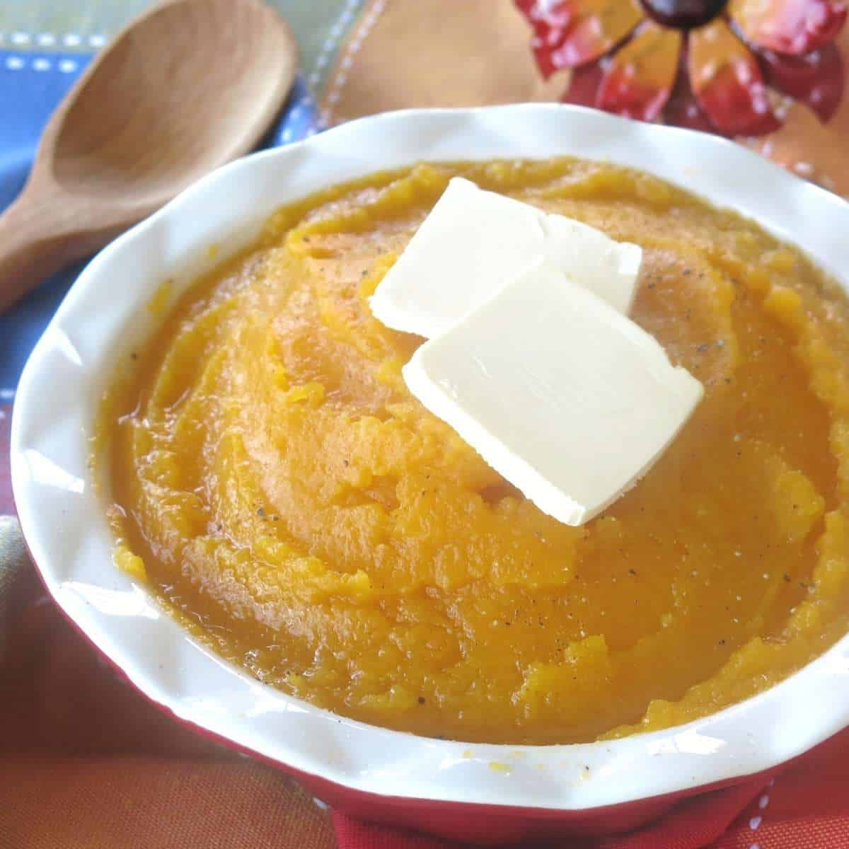 Mashed butternut squash cooked in a crock-pot topped with butter tabs in a serving bowl.