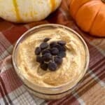 Whipped pumpkin cottage cheese in a cup topped with chocolate chips with 2 pumpkins behind it.