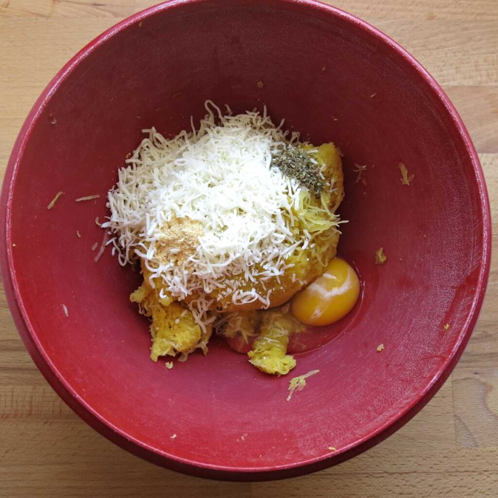 Pressed spaghetti squash strands, cheese, egg, and spices in a red bowl.