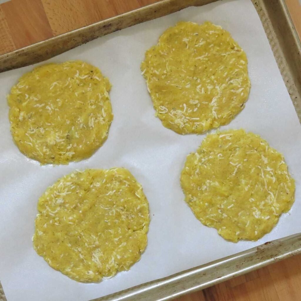 Four uncooked spaghetti squash pizza crusts on a baking sheet lined with parchment paper.