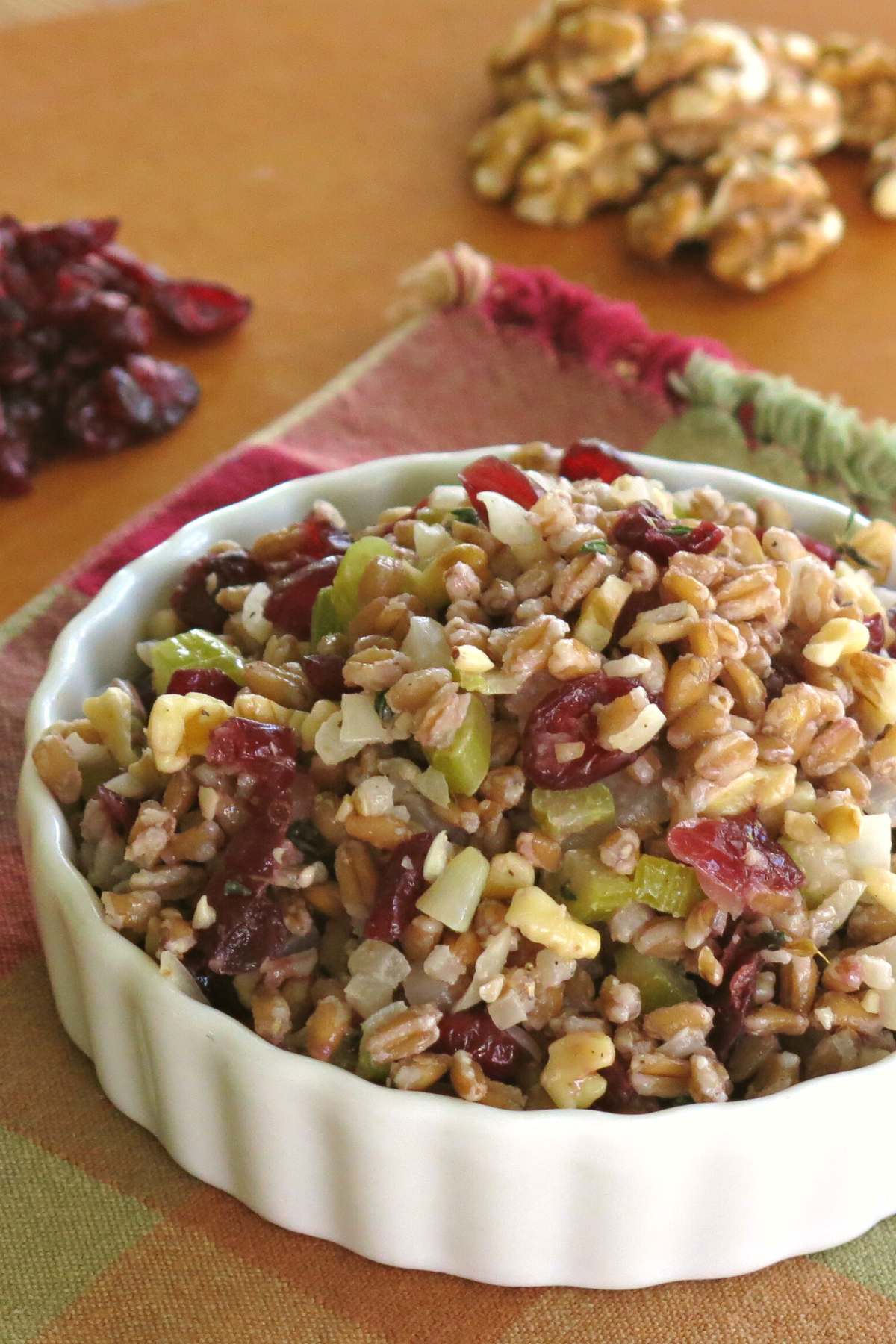 Farro Stuffing Pilaf in a serving bowl with walnuts and cranberries behind it.