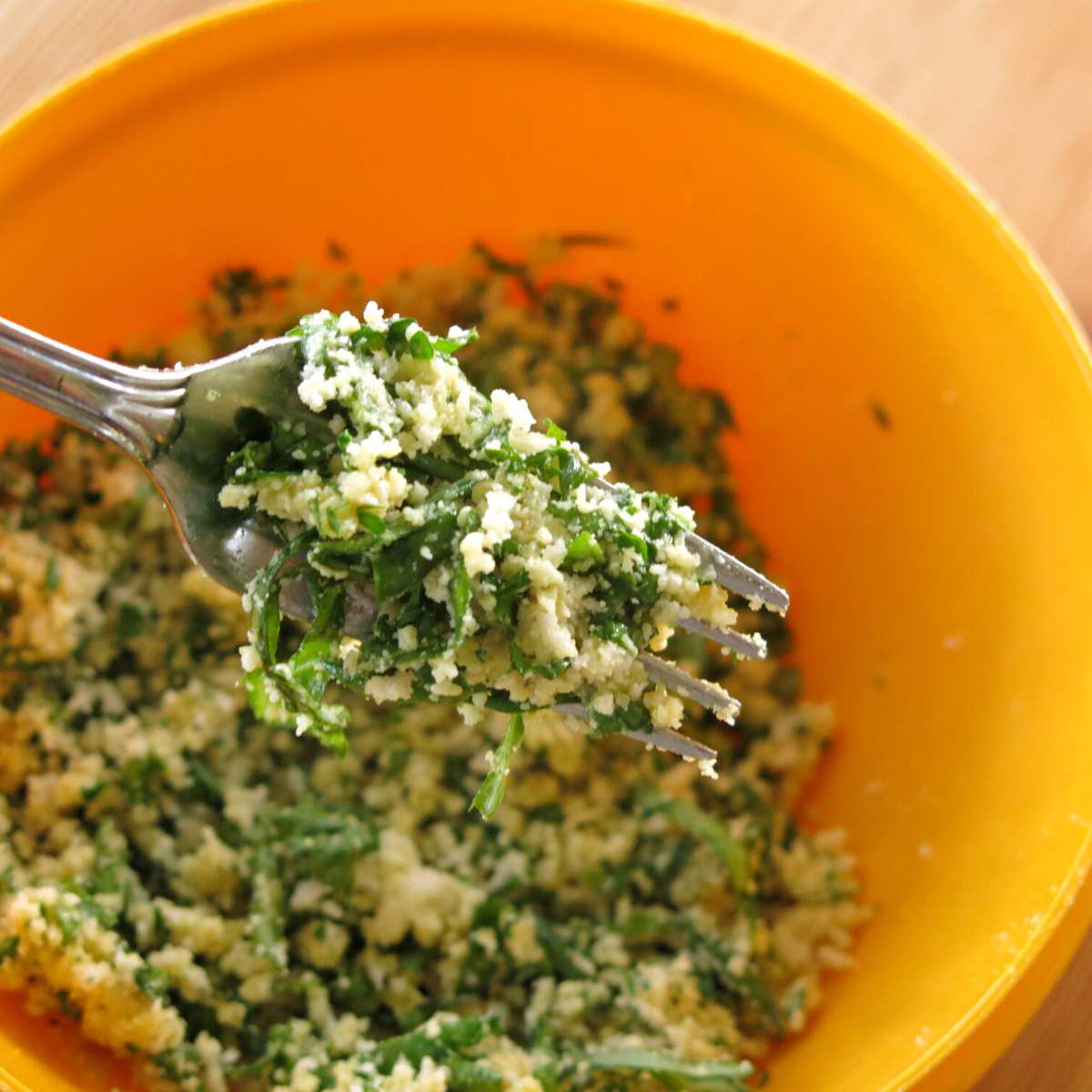 Fork holding fresh herb and Parmesan breading over a bowl with more.