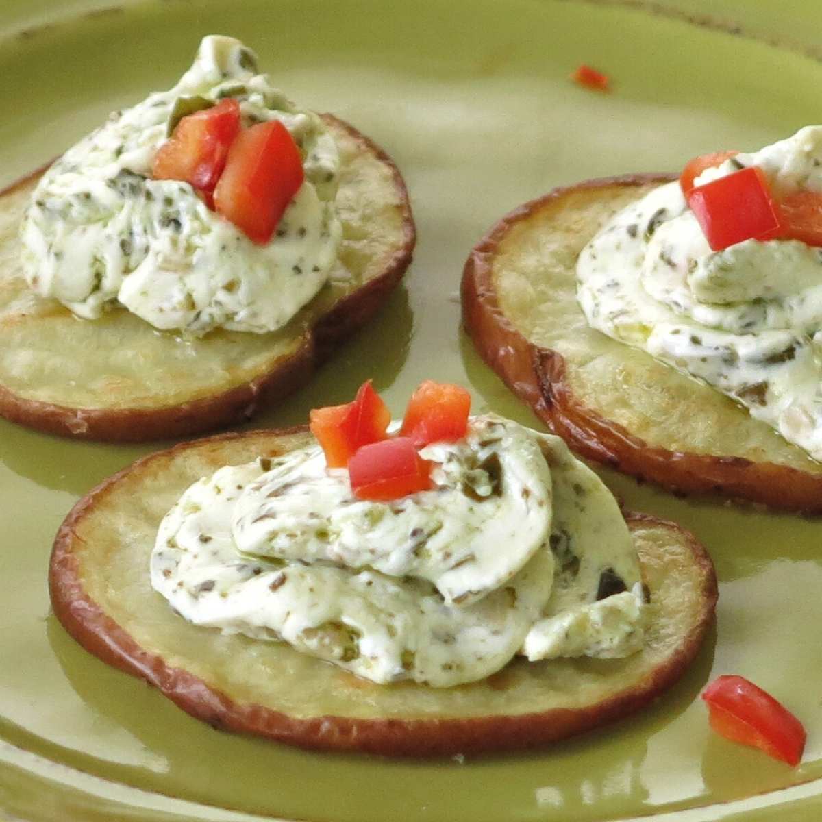 Three roasted potato crostini rounds topped with pesto and cream cheese mixture.