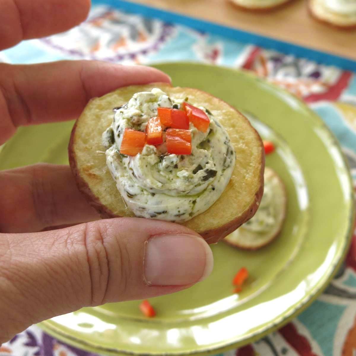 Hand holding a roasted potato appetizer topped with pesto and cream cheese.