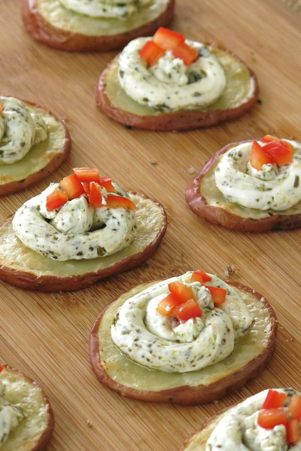 Roasted potato slices with pesto and cream cheese mixture on top lined up on a board.