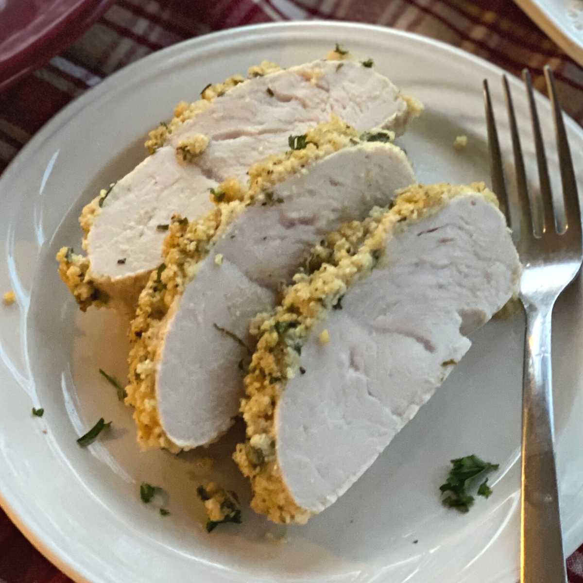 Slices of turkey tenderloin with herb crust on a plate with a fork.