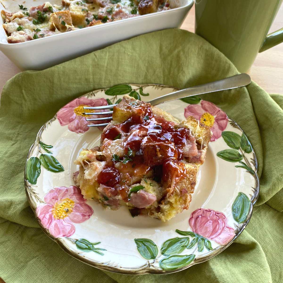 Serving of Monte Cristo casserole on a plate with casserole dish behind it.