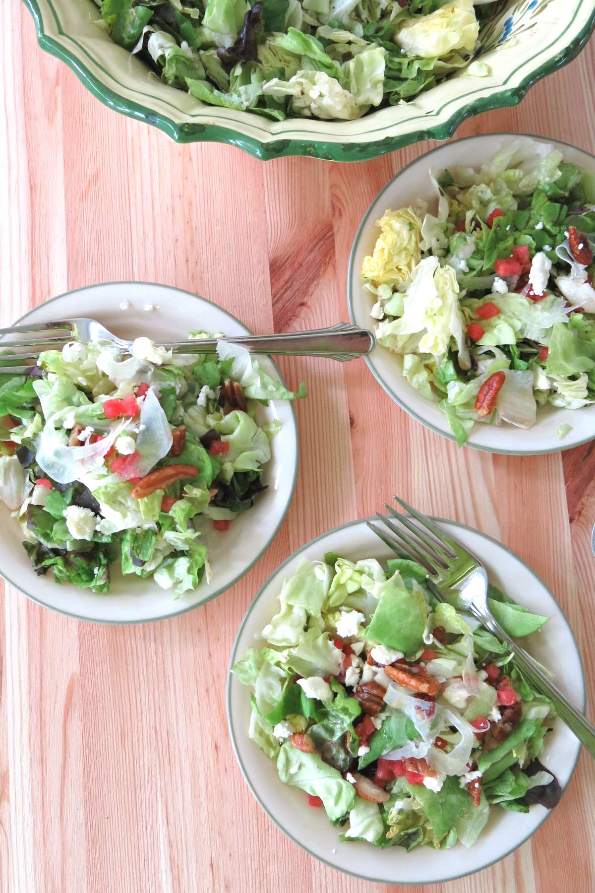 Three small side salads of the fancy salad with shaved fennel, candied pecans, watermelon, and feta cheese on plates with the bowl behind it.