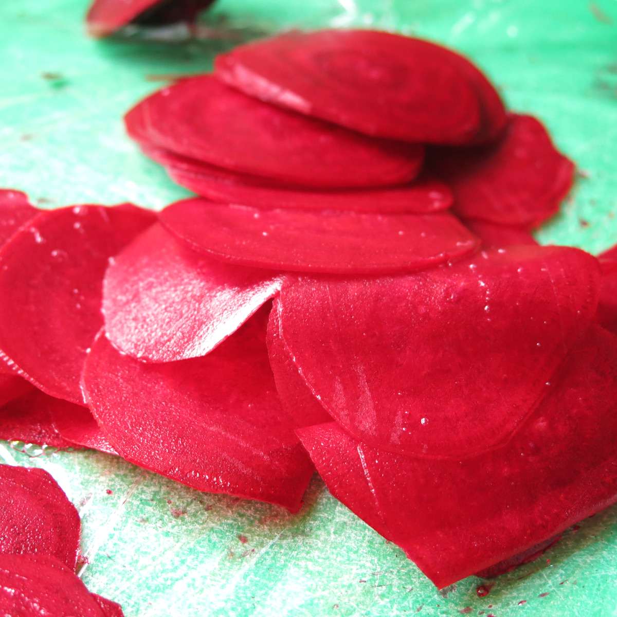 Raw slices of beets about 1/16 inches thick on a cutting board.