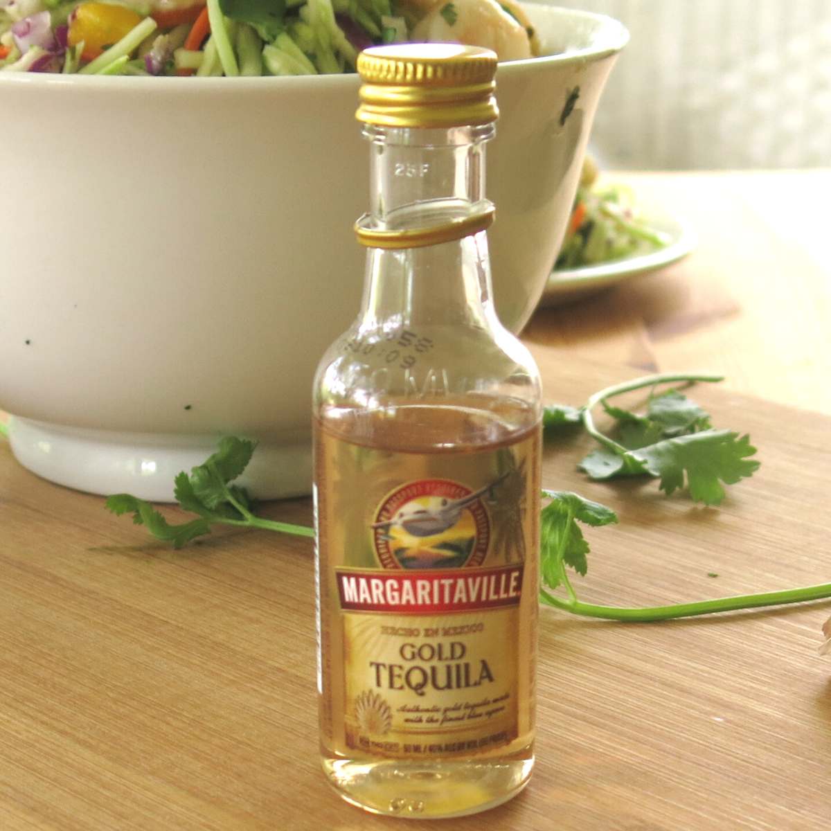 Very small bottle of Margaritaville Gold Tequila in front of bowl with shrimp.