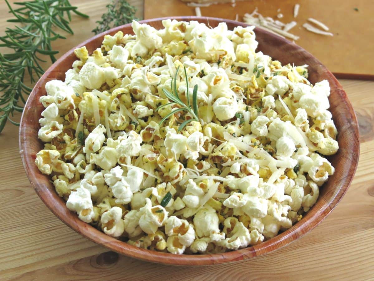 Parmesan herb popcorn in a brown bowl with rosemary sprigs and shredded cheese in the background.