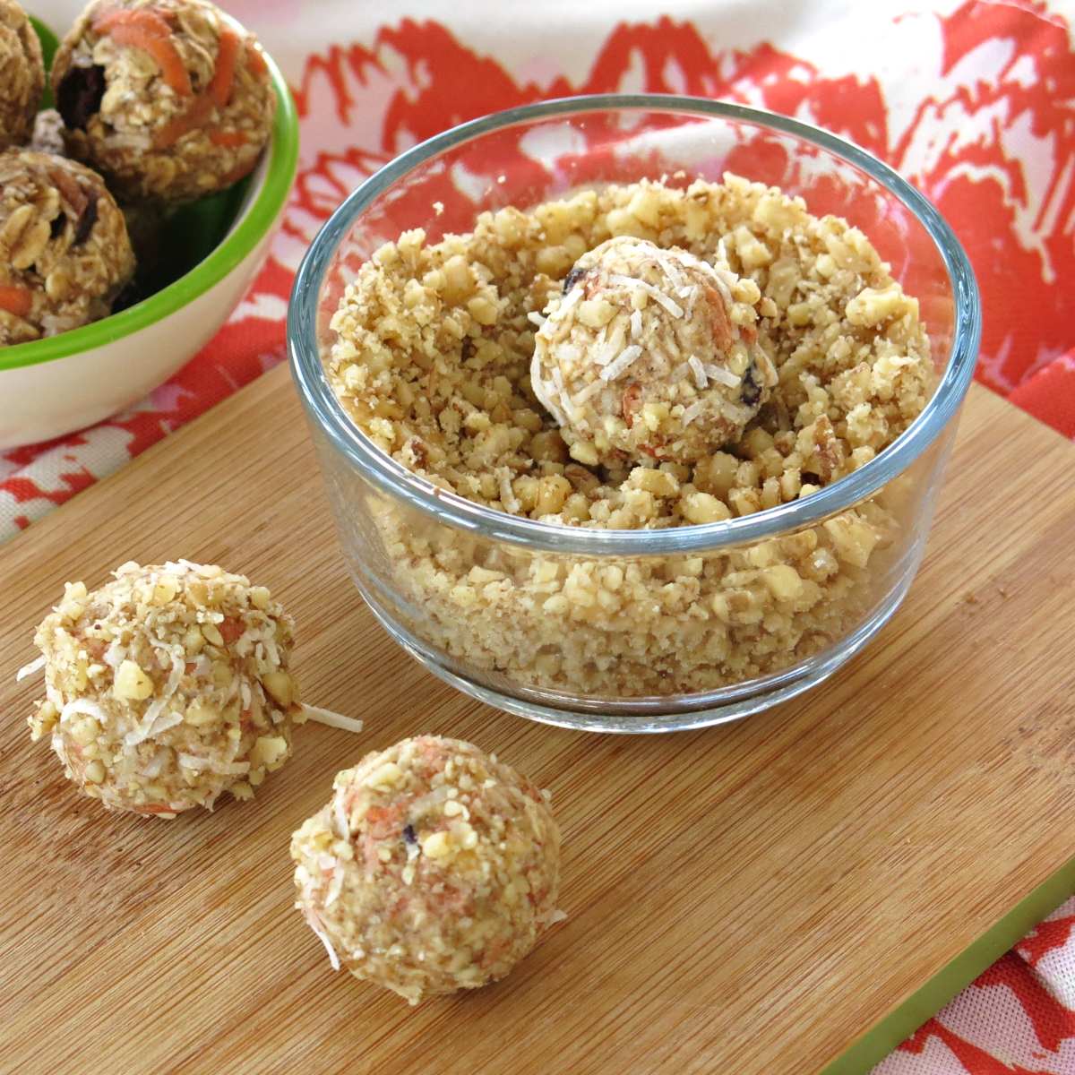 Carrot cake energy balls that have been rolled in coconut and walnuts on a cutting board and one in a bowl.