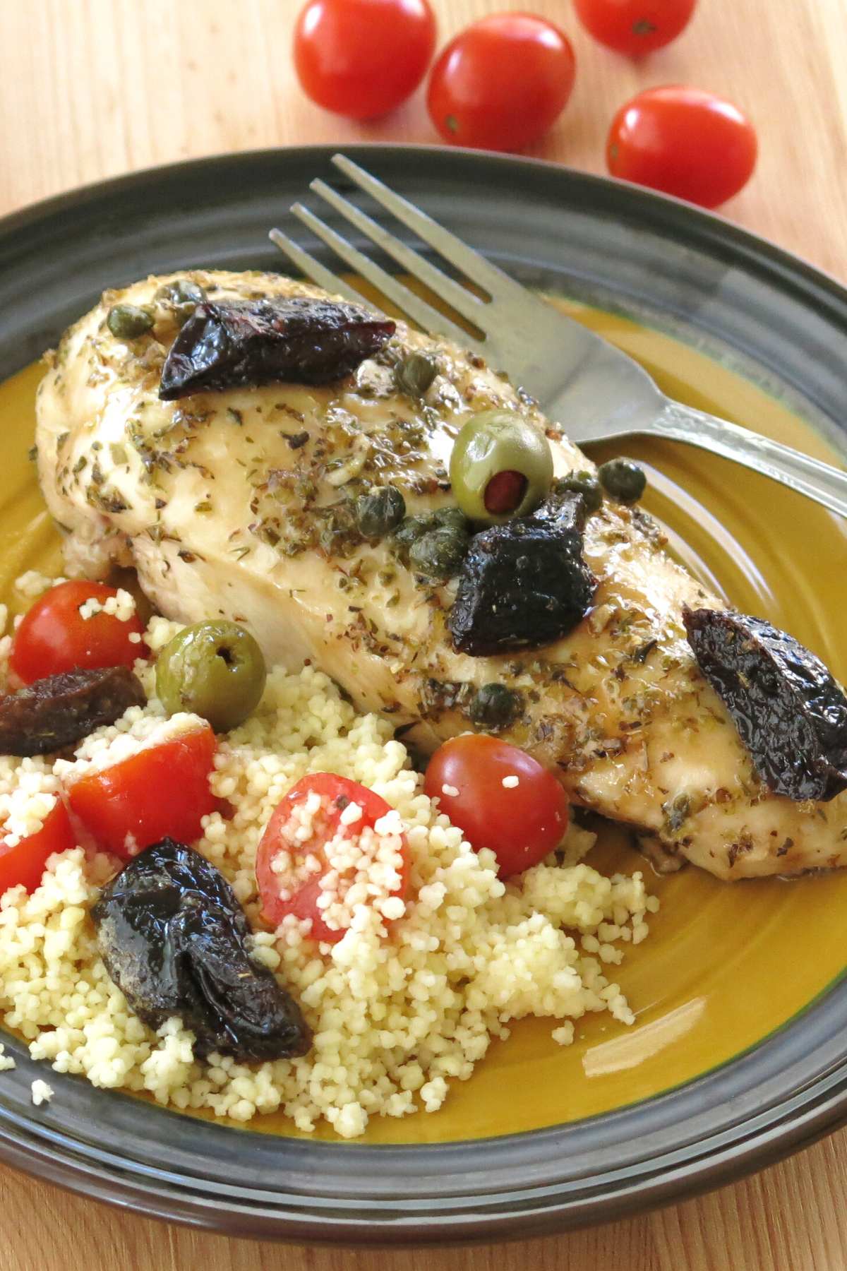 Plate with chicken marbella made with boneless breasts topped with prunes, green olives, and capers with couscous next to it.