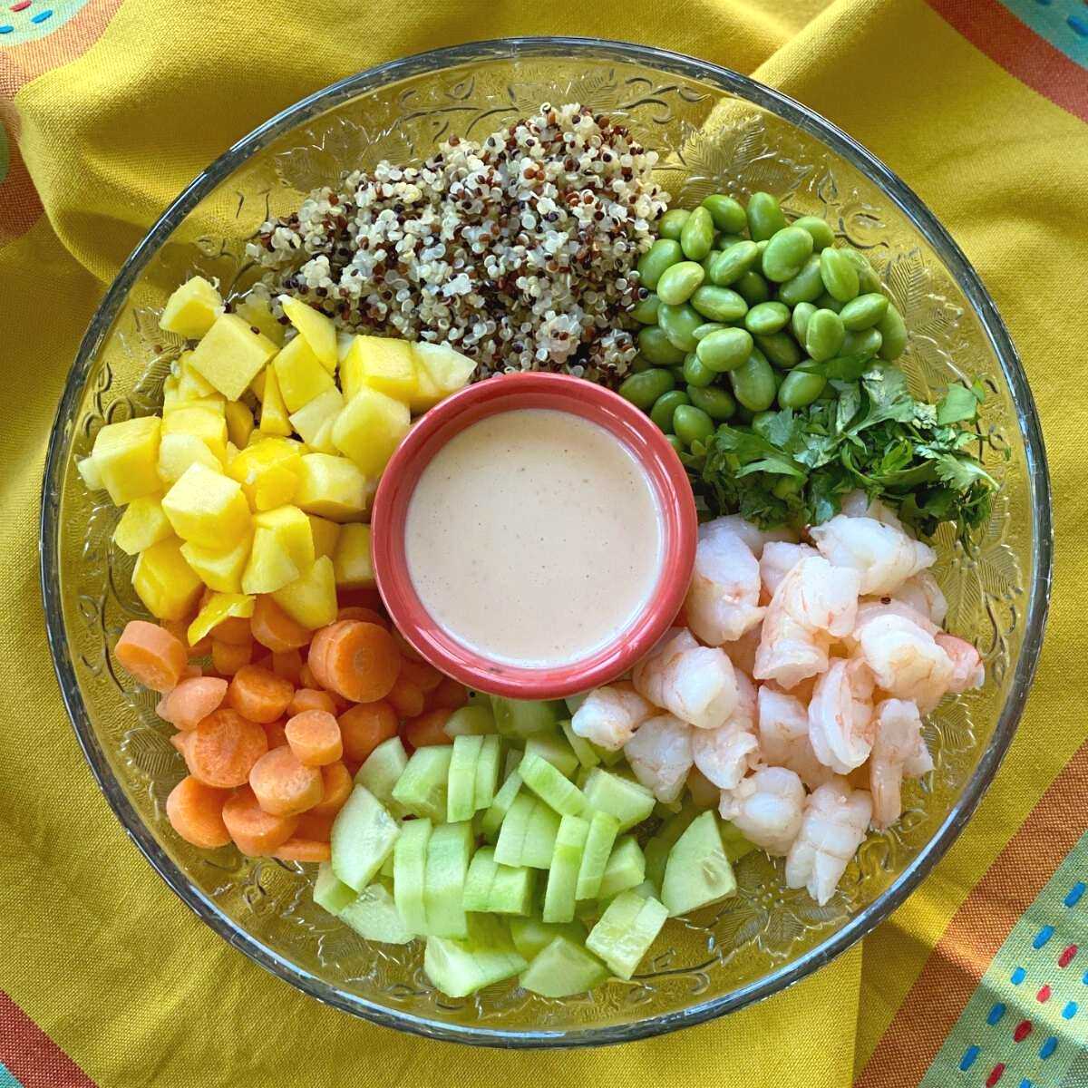 Shrimp poke bowl ingredients not combined in a bowl: shrimp, rice, edamame, carrots, cucumbers, mango, cilantro, poke sauce in the middle.