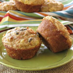 Two pineapple carrot muffins on a plate with more in a basket behind them.