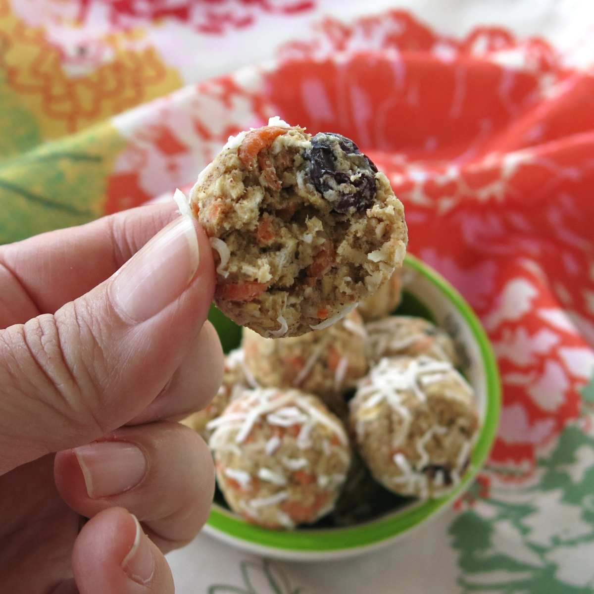 Fingers holding a raw carrot cake energy ball with a bit removed.