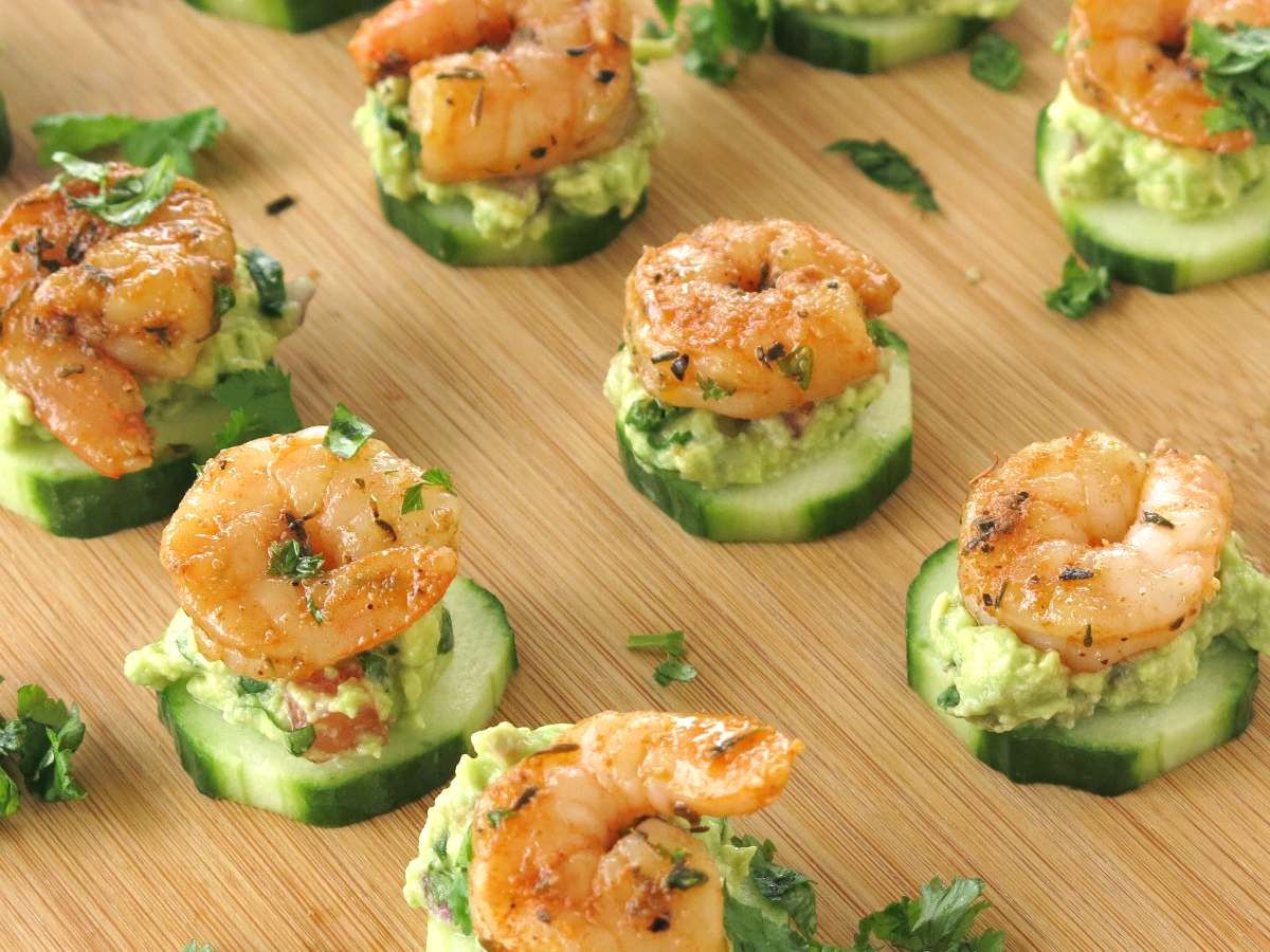 Lines of shrimp layered on top of guacamole on a slice of cucumber.