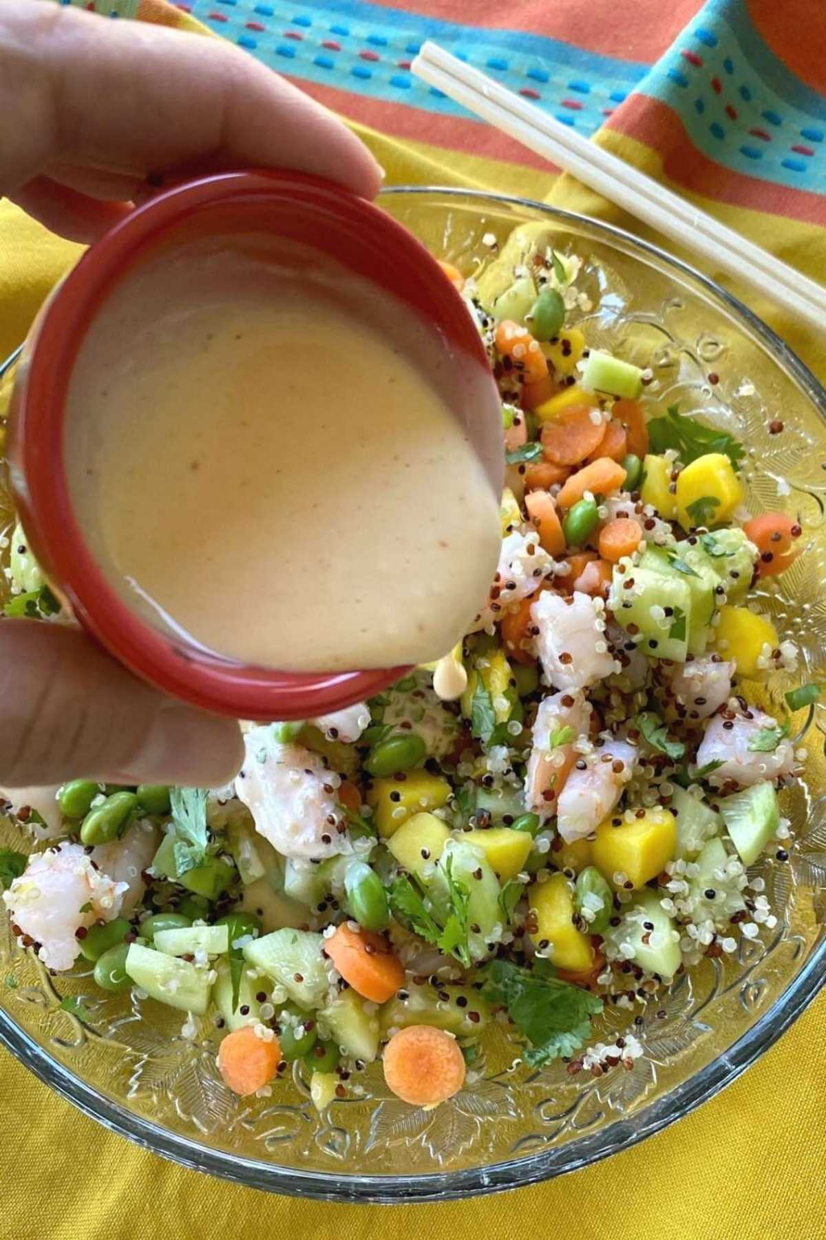 Creamy poke sauce being poured over a poke bowl with shrimp.