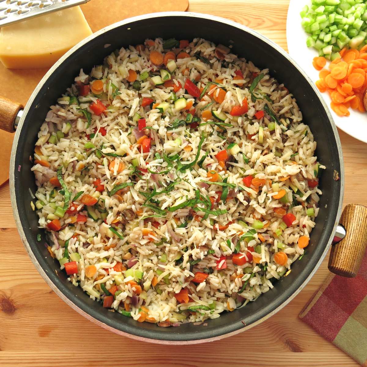 Vegetable rice pilaf in a skillet with carrots and celery next to it.