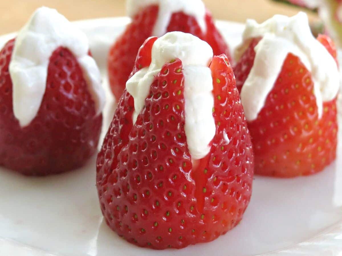 Four no-bake cheesecake stuffed strawberries on a plate.