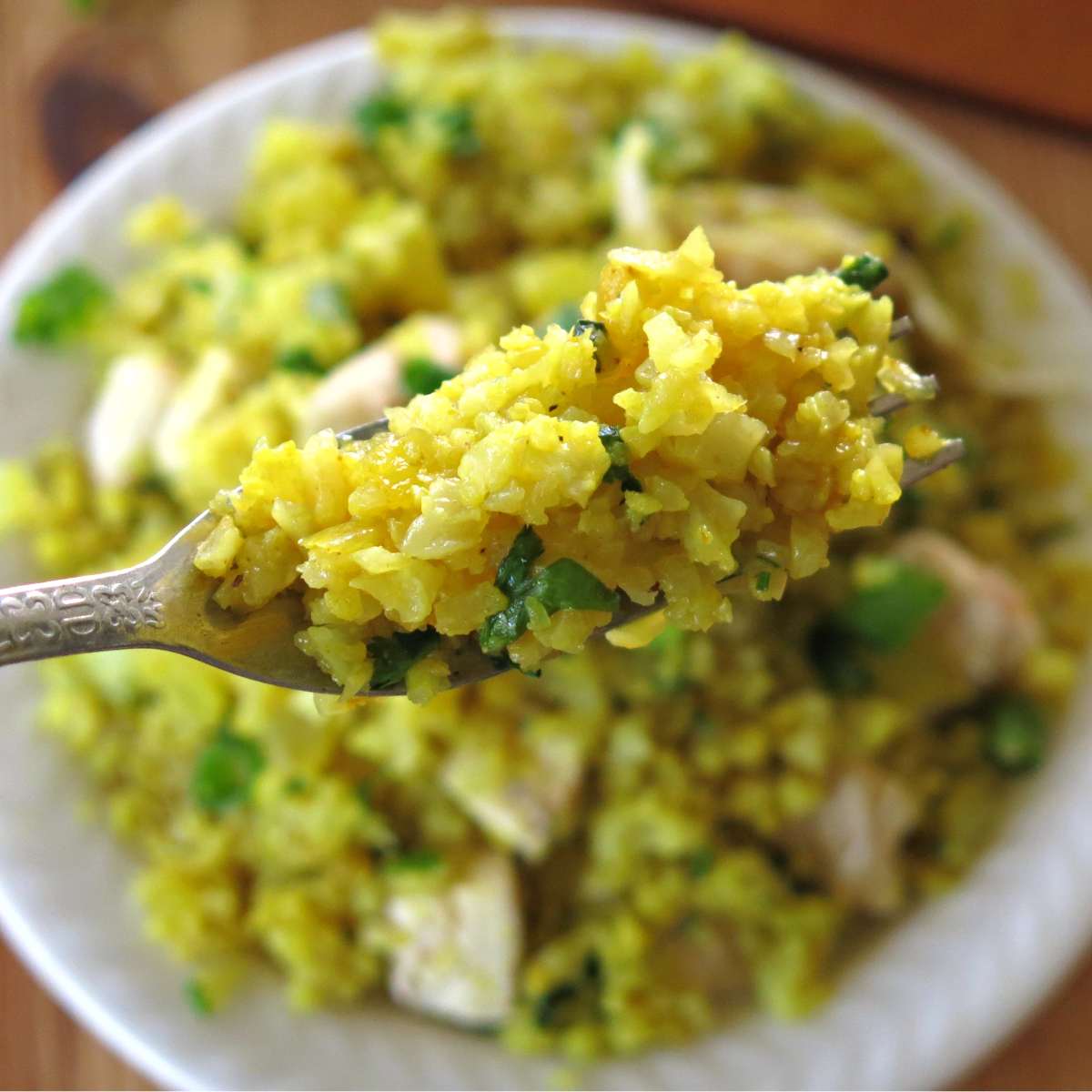 Curry cauliflower rice on a fork with more in a bowl below it.