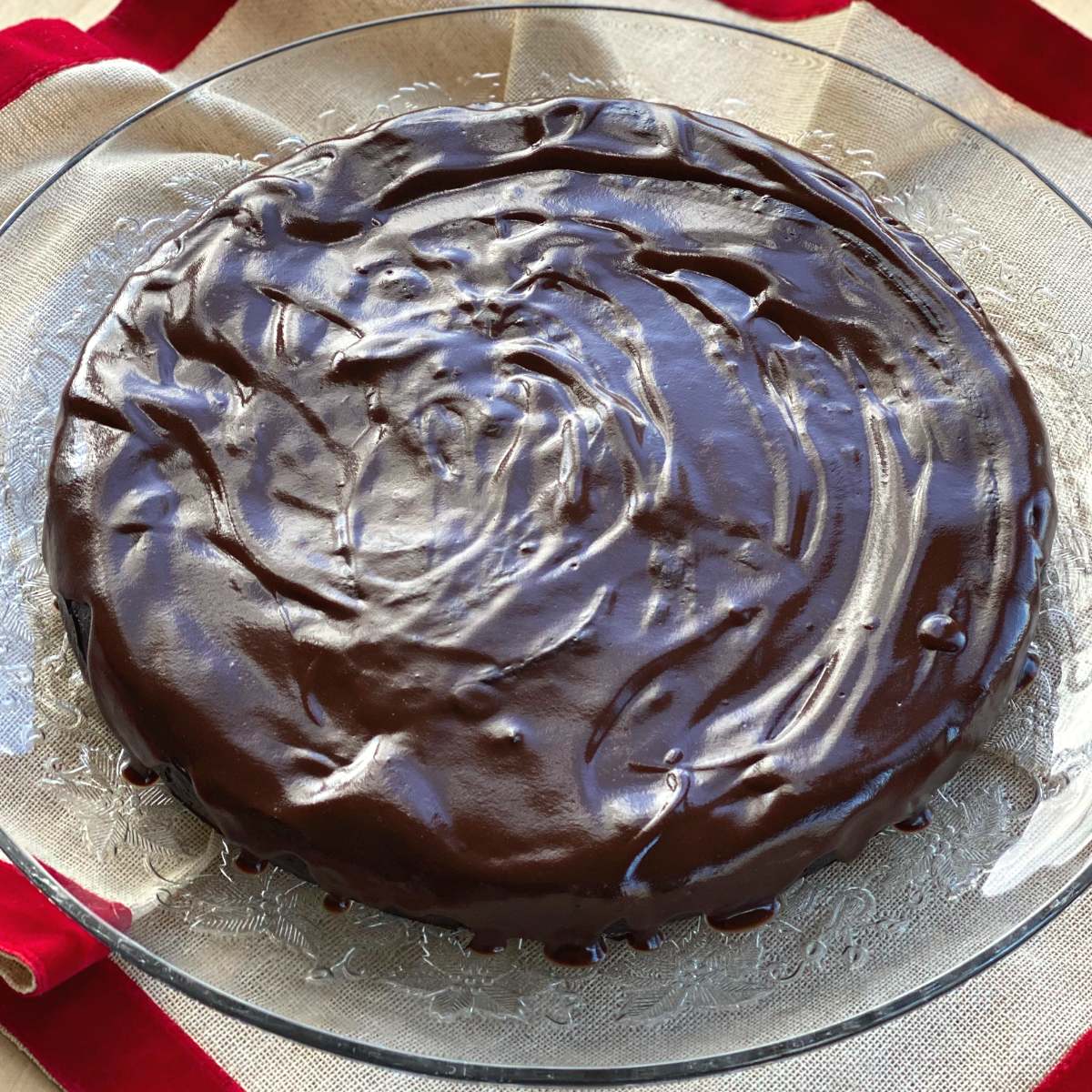 Flourless chocolate cake with ganache on a glass cake plate.