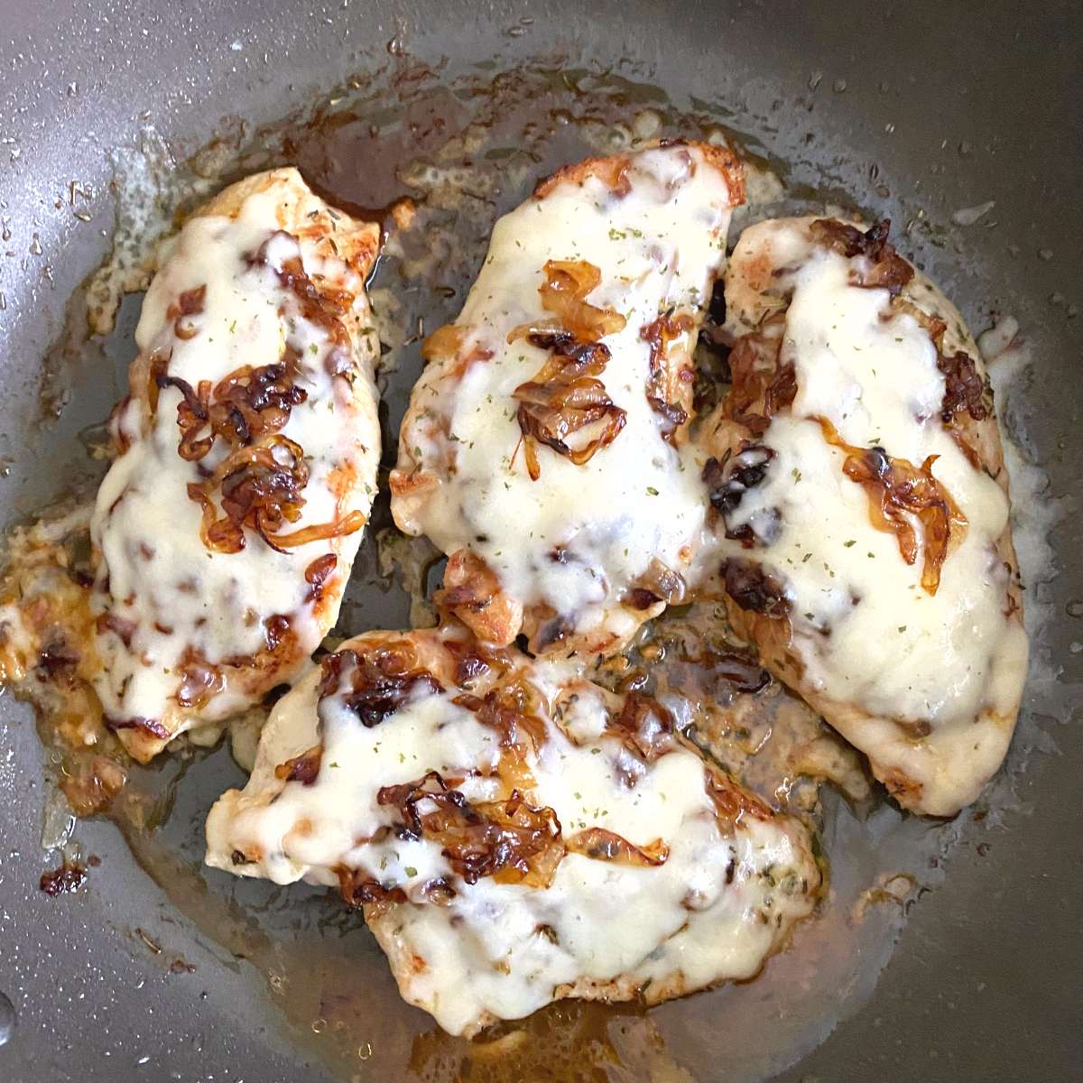 Finished French Onion Chicken in skillet with melted Guryére cheese and extra caramelized onions on top.