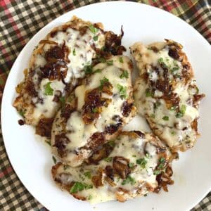 Skillet French Onion Chicken topped with Gruyére cheese and caramlized onions on a serving plate.