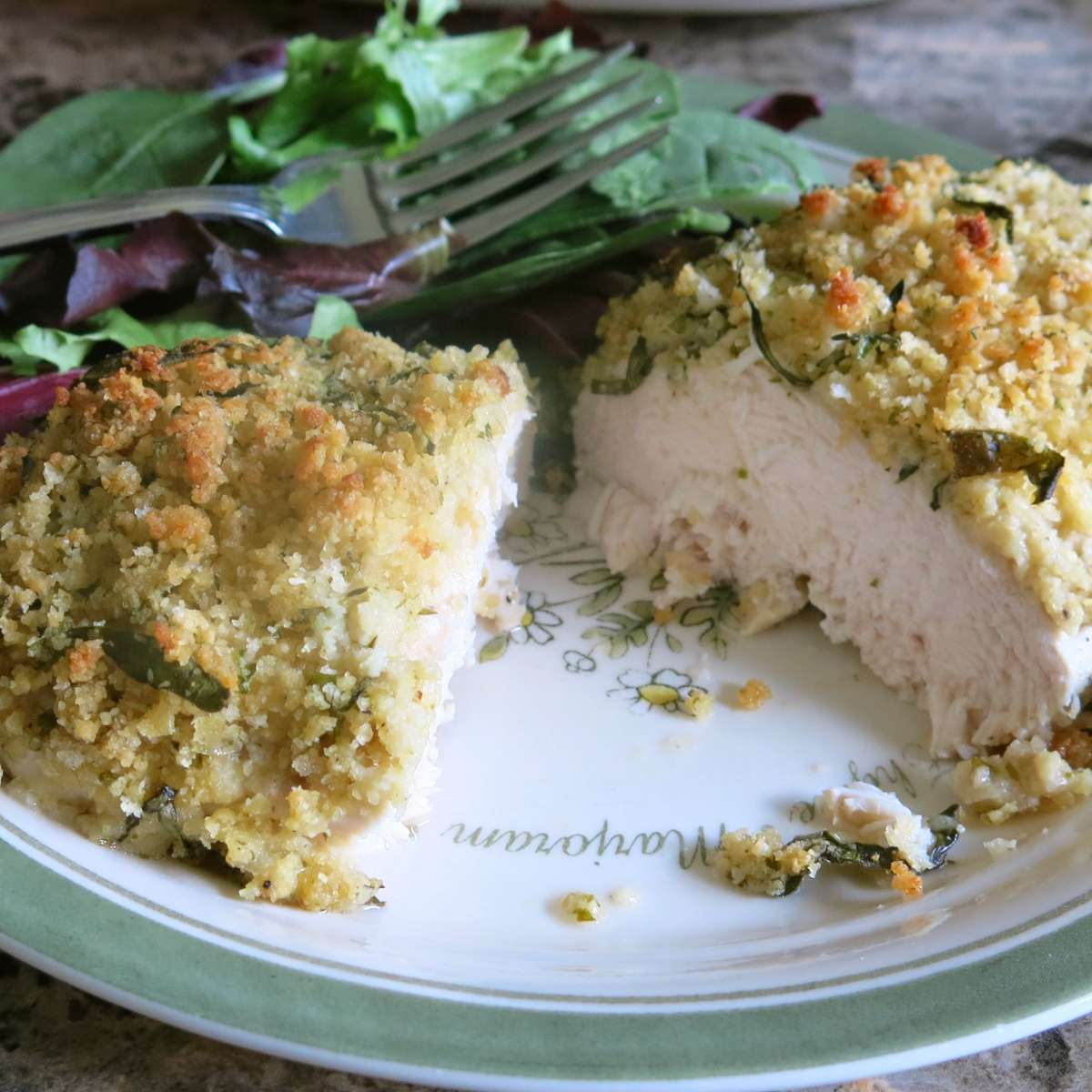 Baked herb crusted chicken breast cut in half to expose juicy center on a plate.