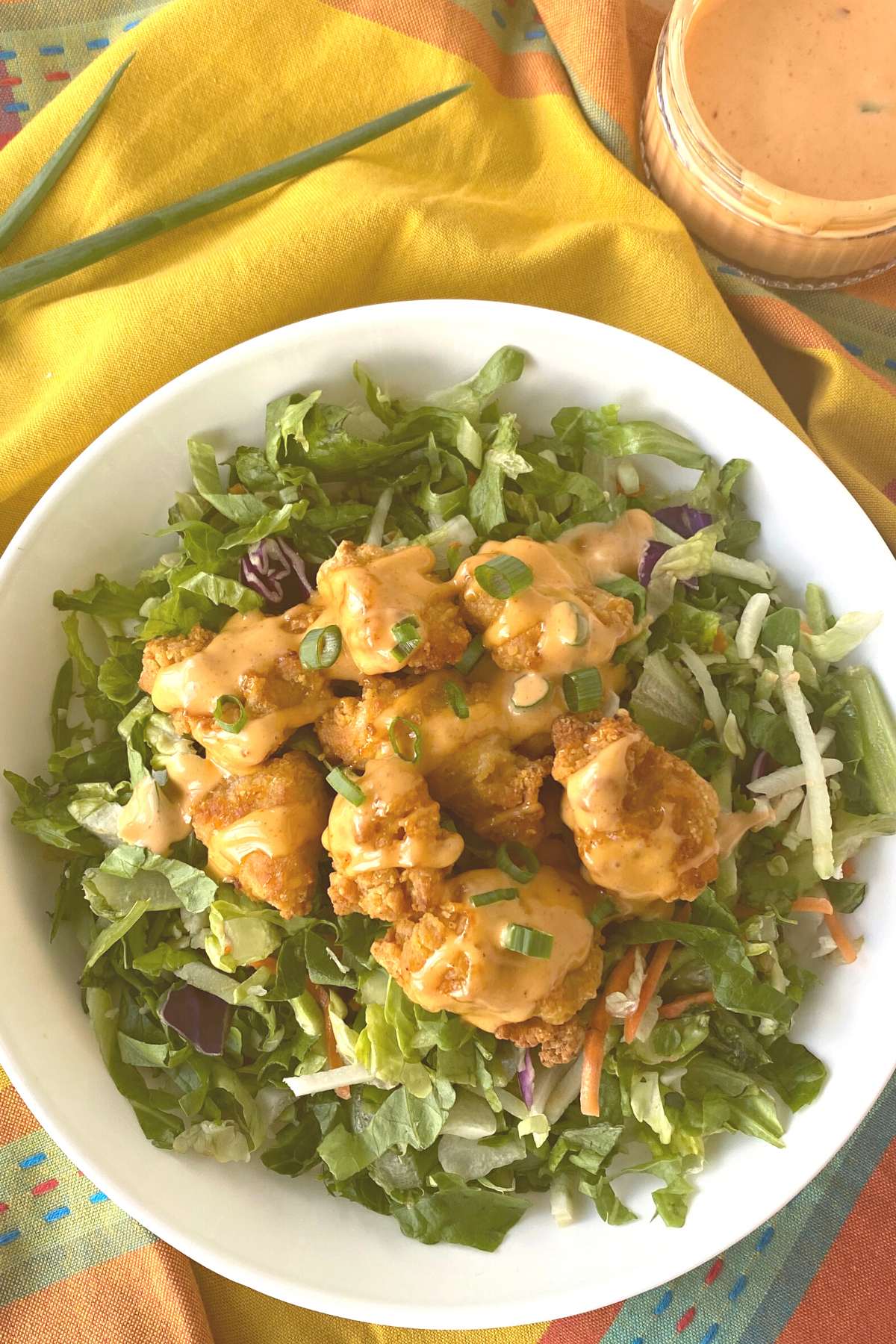 Chicken nuggets covered with homemade bang bang sauce on top of salad greens.