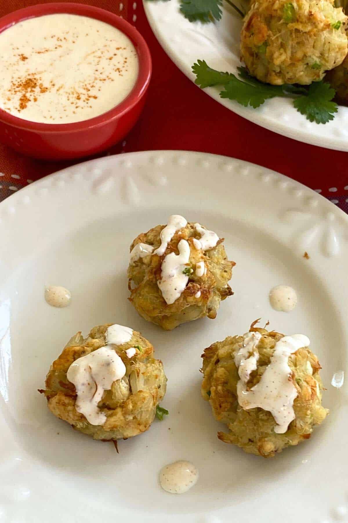 Three crab bites drizzled with aioli on a plate.