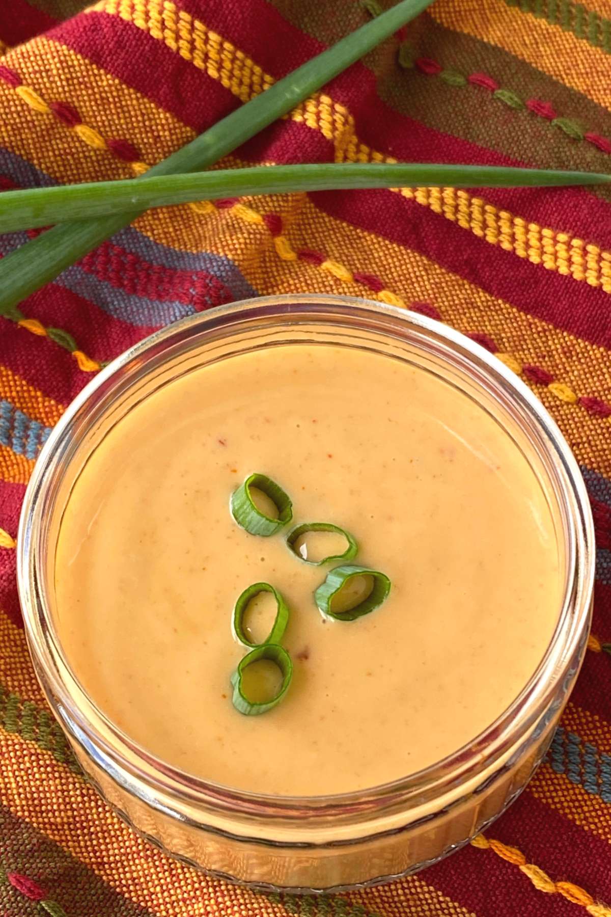 Easy bang, bang sauce in container garnished with green onion slices with more spring onion behind it.