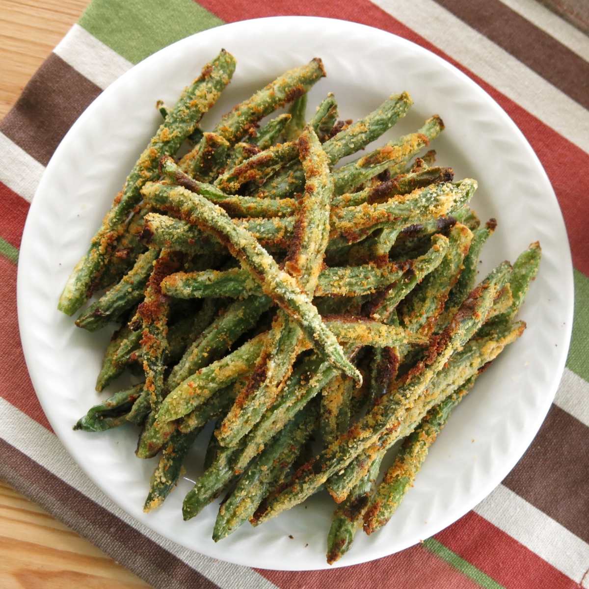 Baked green bean fries appetizer coated in Parmesan cheese on a plate.