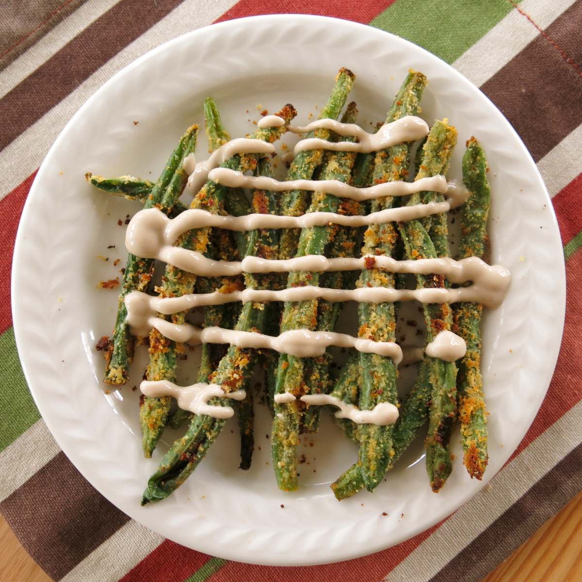 Keto green bean fries stacked on a plate with yogurt sauce drizzled over the top.