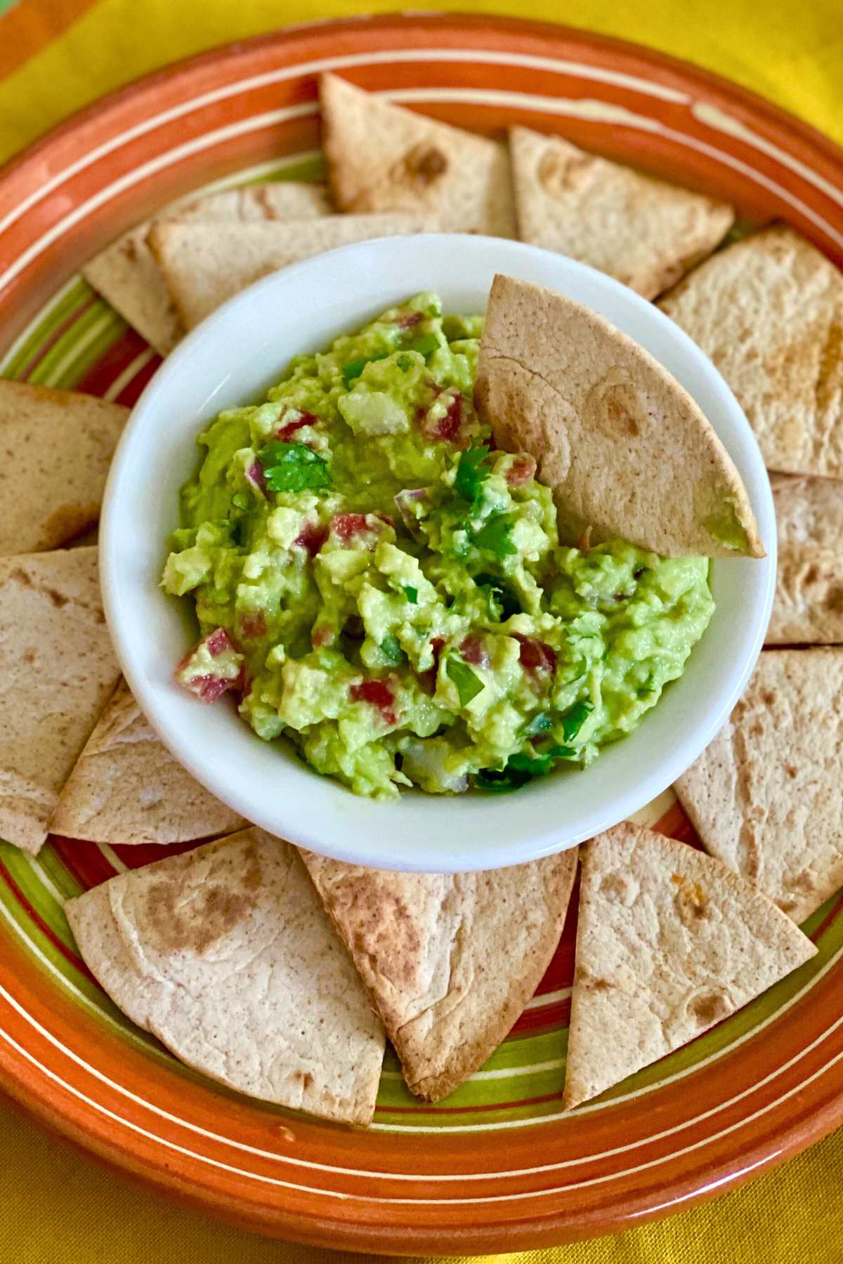 Chip dipped in bowl of guacamole dip with more chips surrounding it.
