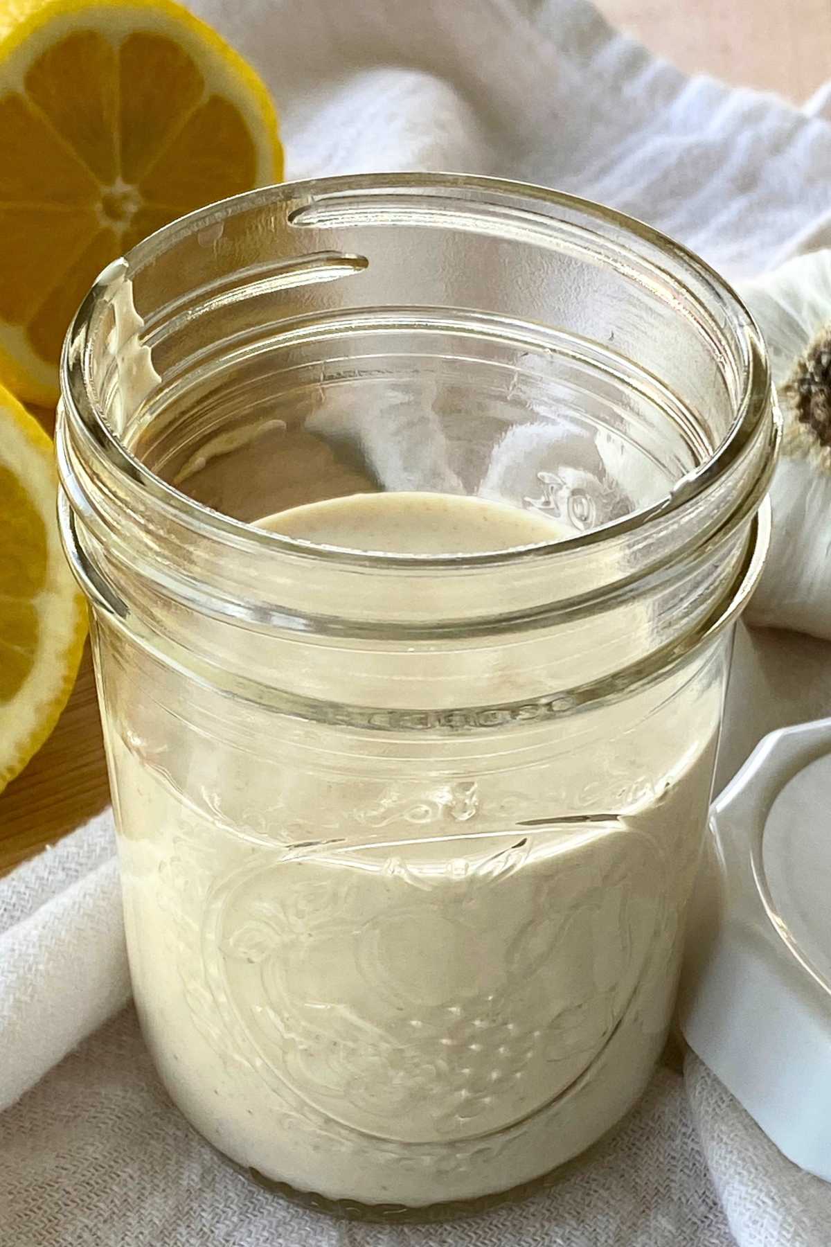 Easy lemon garlic aioli sauce in a small mason jar with lid, lemon, and head of garlic next to it.