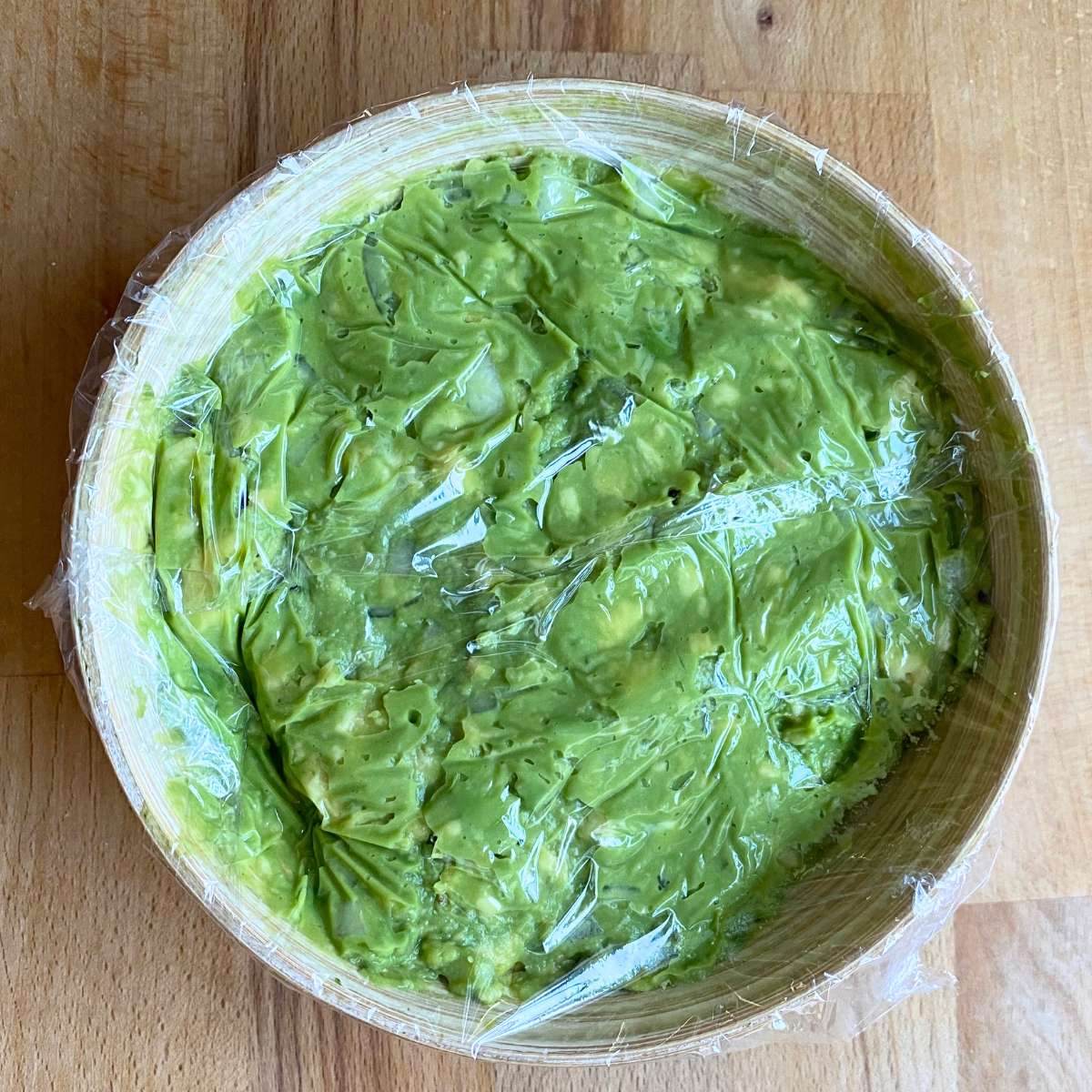 Simple guacamole dip in a bowl with plastic wrap covering the surface for storage.