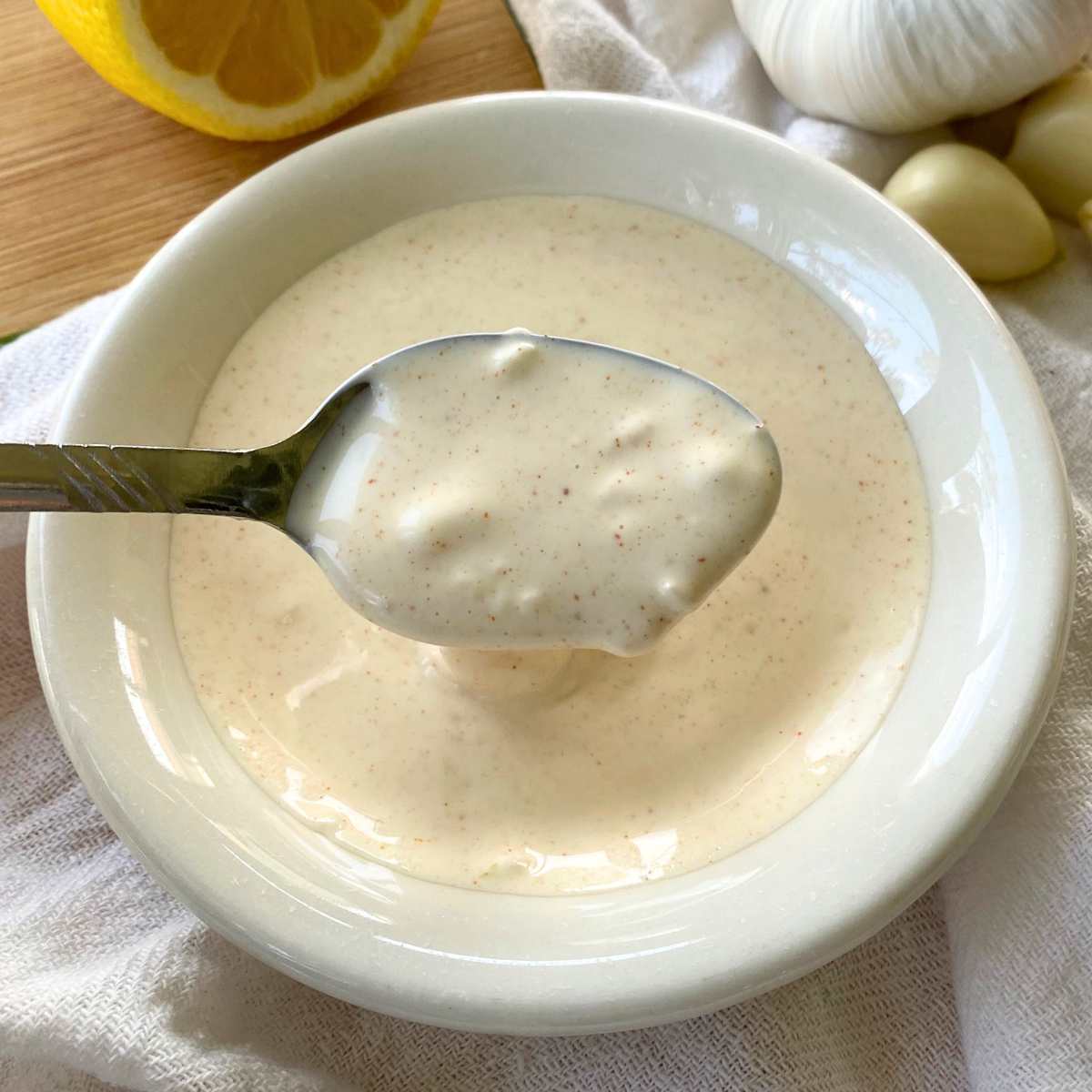 Spoon lifting homemade lemon garlic aioli out of a small bowl.