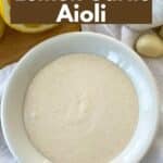 Lemon garlic aioli in a bowl with a cut lemon and garlic cloves behind it.