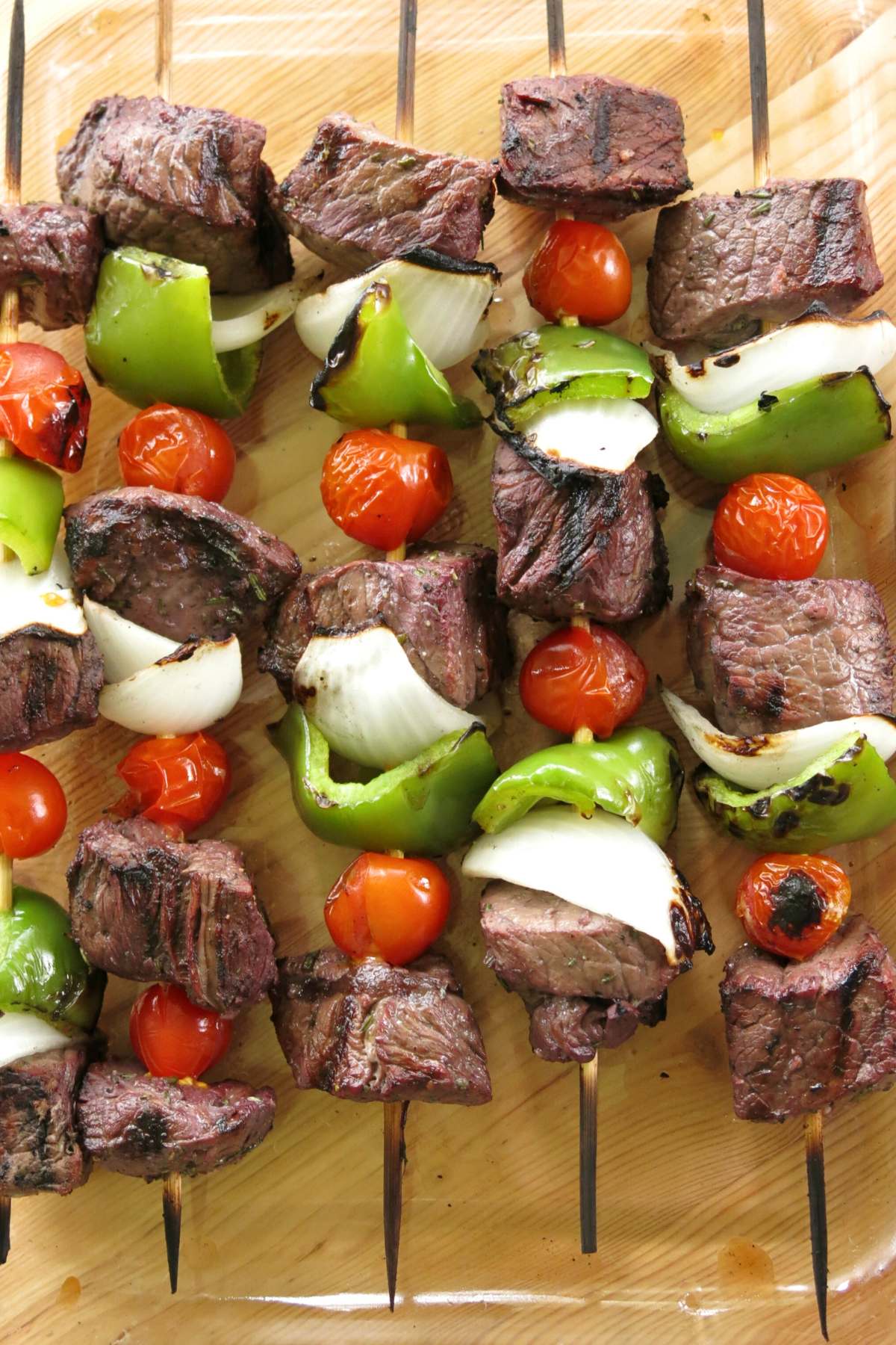 Red wine marinated steak kabobs with onion, pepper, and tomates on the skewers in a glass dish.