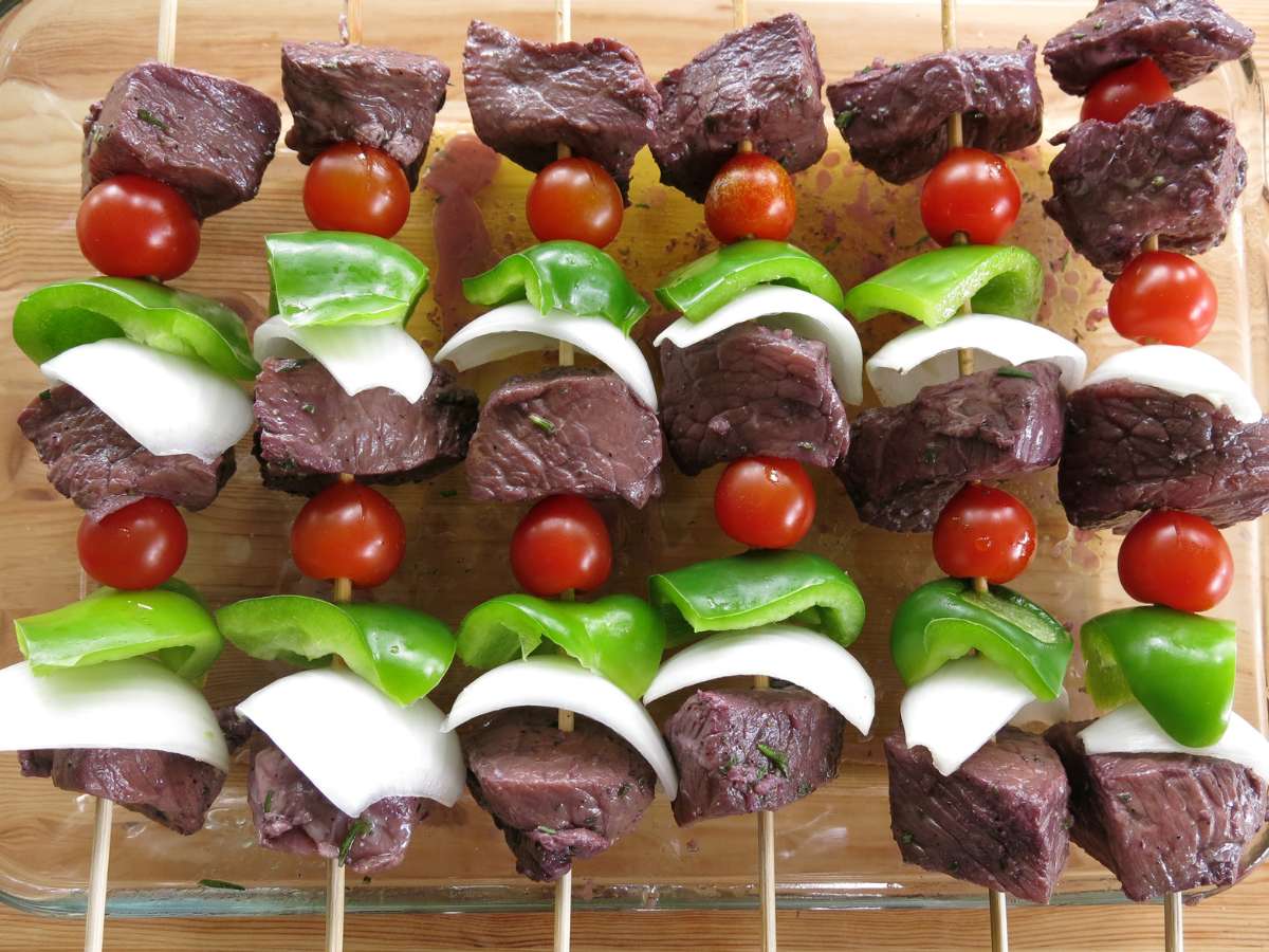 Uncooked vegetables and red wine marinated steak shish kabebs on wooden skewers.