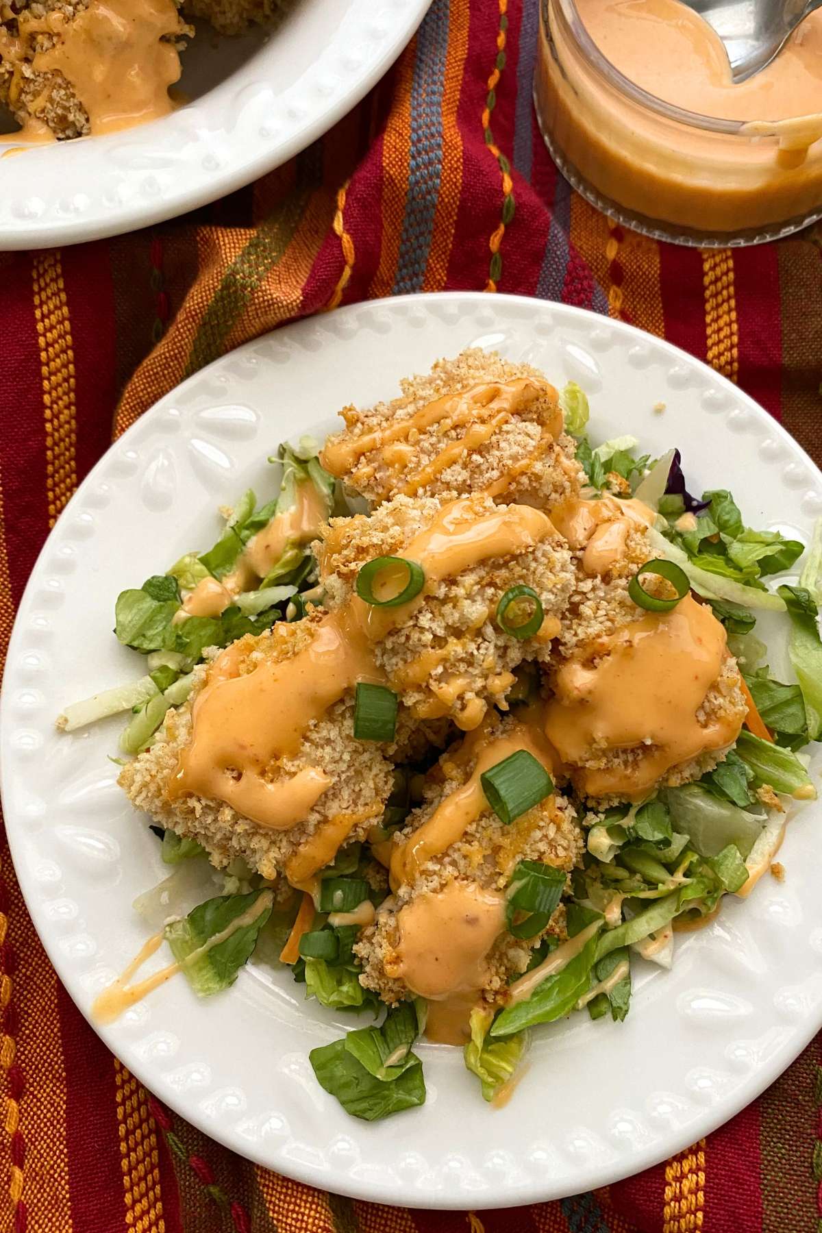 Baked bang bang chicken drizzled with sauce on a plate of crispy salad greens.