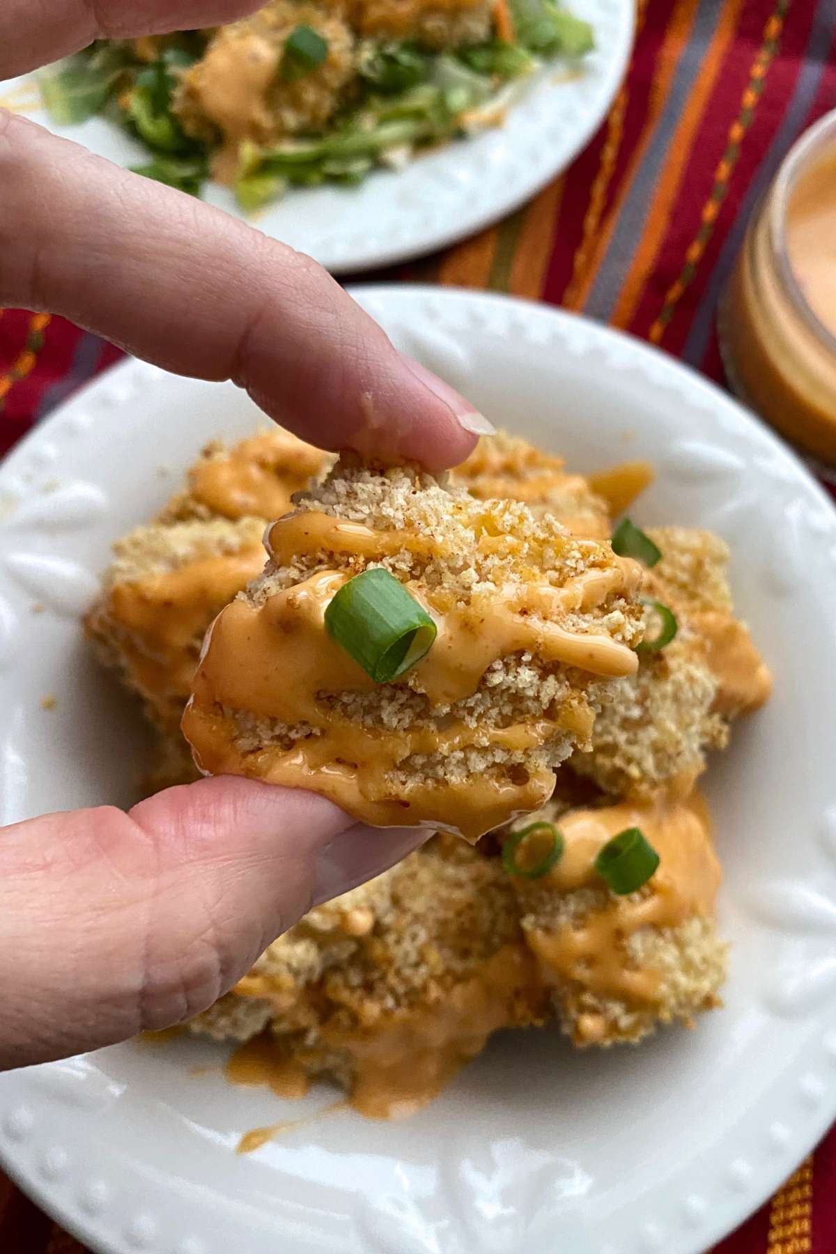 Fingers holding a nugget of baked bang bang chicken.